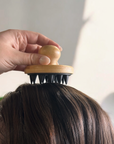 hand holding bamboo and silicone massager on head of brown hair