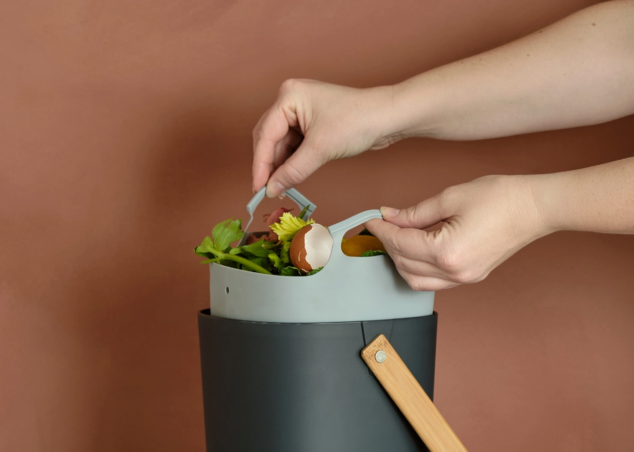 hands pulling grey compost bin liner out of black composter on terracotta background 